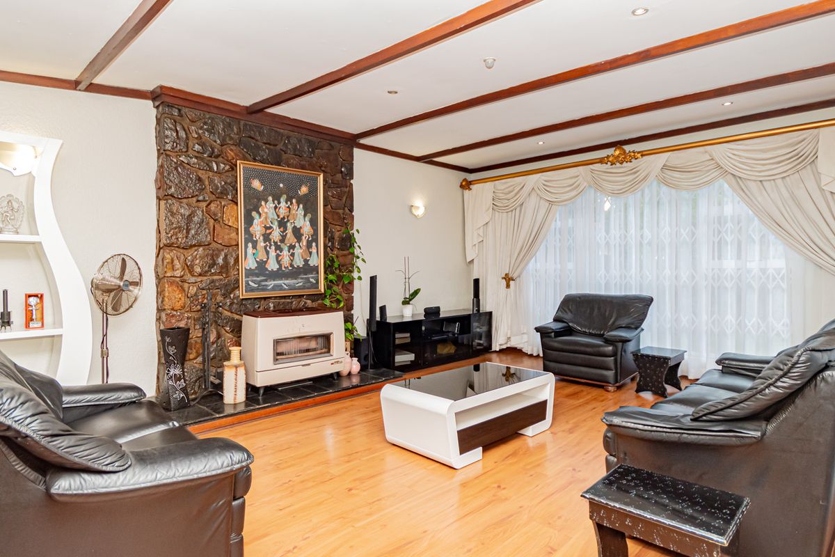 Spacious living room featuring a prominent stone fireplace, exposed timber ceiling beams, and warm laminate flooring, creating a cozy and traditional atmosphere.