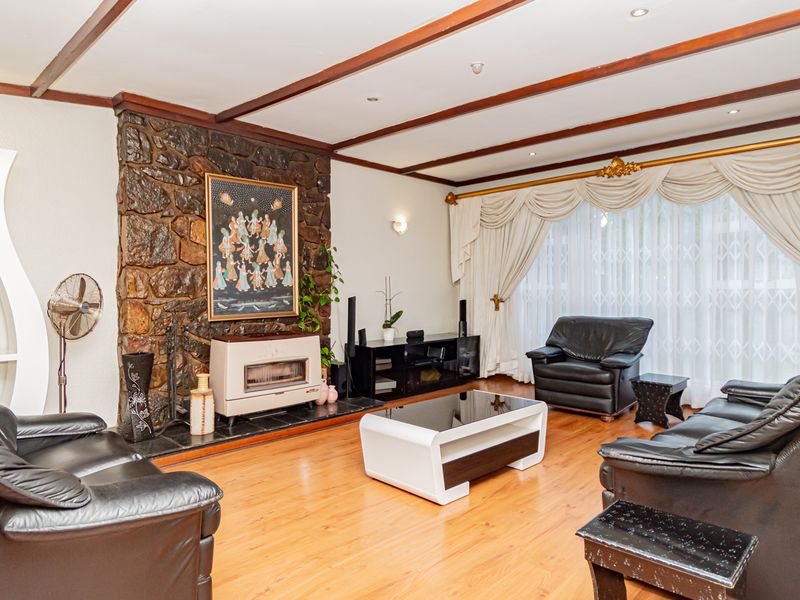 Spacious living room featuring a prominent stone fireplace, exposed timber ceiling beams, and warm laminate flooring, creating a cozy and traditional atmosphere.