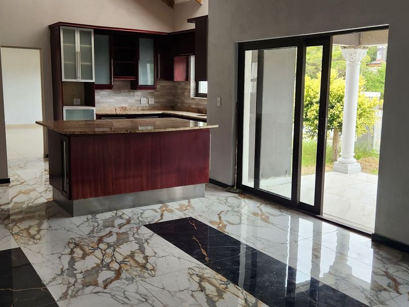 Open-plan living and kitchen area featuring marble-effect tiled flooring, dark wood cabinetry, and sliding glass doors leading to an outdoor patio.