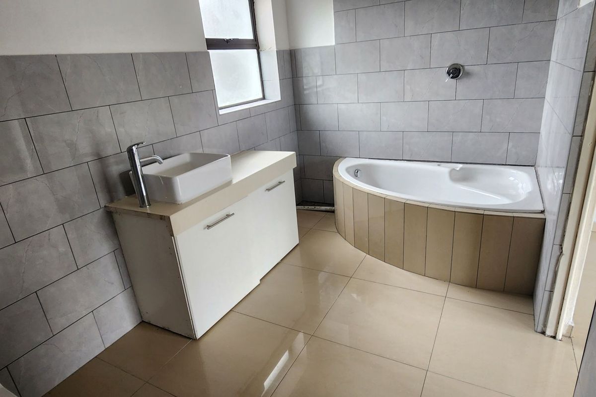 A functional bathroom featuring a corner bathtub, vanity cabinet with vessel sink, and neutral grey wall tiling throughout.