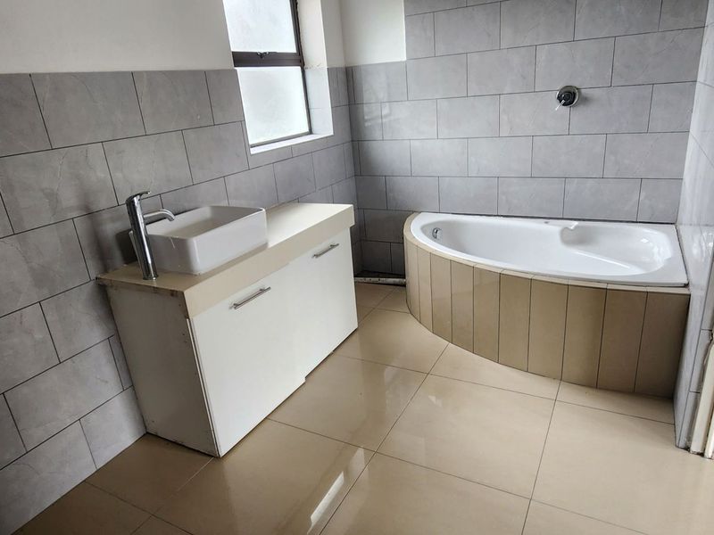 A functional bathroom featuring a corner bathtub, vanity cabinet with vessel sink, and neutral grey wall tiling throughout.