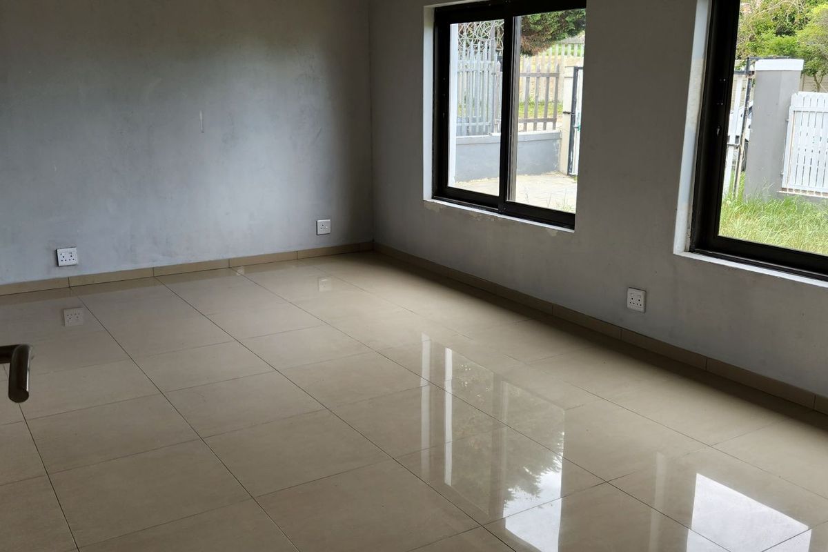 An empty, neutral living area featuring tiled flooring and large aluminium-framed windows, awaiting final finishes and personal touches.