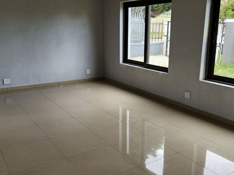 An empty, neutral living area featuring tiled flooring and large aluminium-framed windows, awaiting final finishes and personal touches.