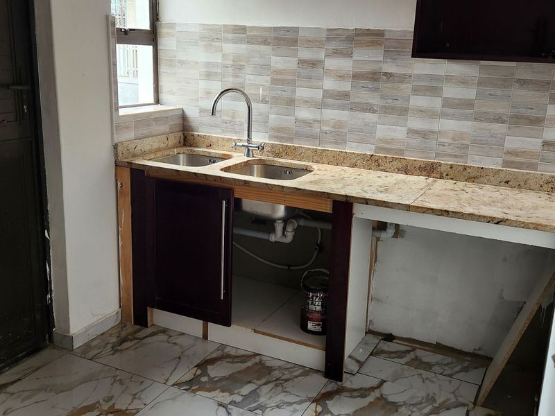 A functional scullery or utility area featuring a double bowl sink, granite countertops, and tiled finishes, currently requiring completion of cabinetry and plumbing fixtures.