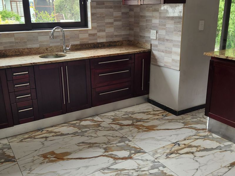 A modern kitchen featuring dark wood cabinetry, granite countertops, a stainless steel sink, and elegant marble-look floor tiles.