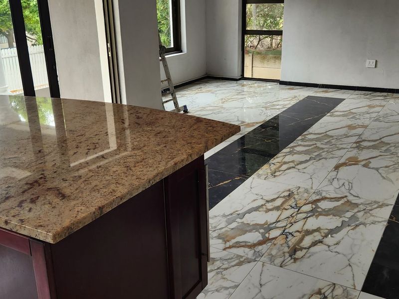 Spacious open-plan living area featuring a granite-topped kitchen island and striking marble-look tiled flooring with black accent detailing, awaiting final finishing touches.