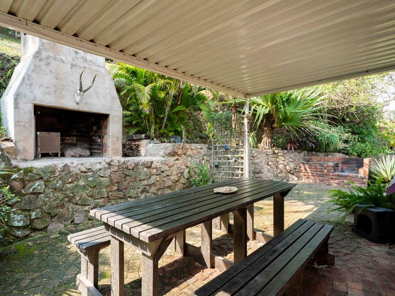 Covered outdoor patio featuring a built-in braai, stone retaining walls, and brick paving, providing a rustic space for outdoor dining and entertainment.