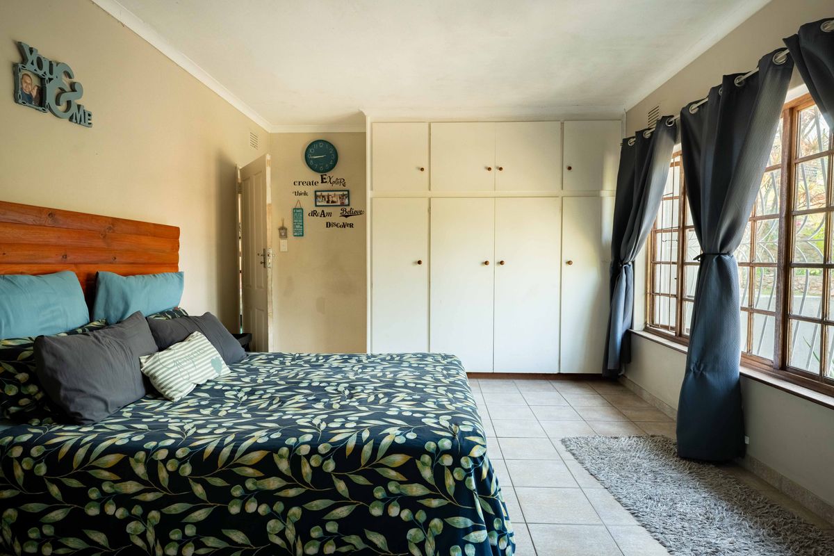 A bedroom featuring built-in cupboards, tiled flooring, and a window with security bars.