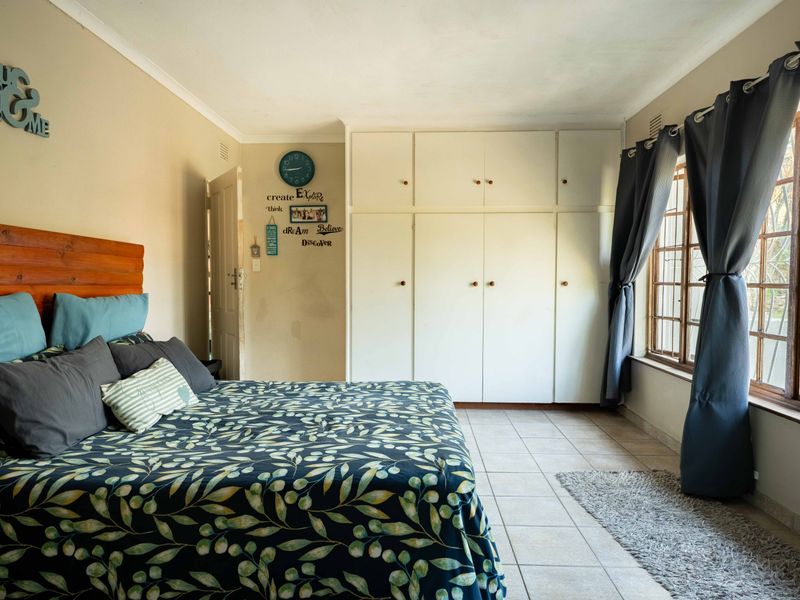 A bedroom featuring built-in cupboards, tiled flooring, and a window with security bars.