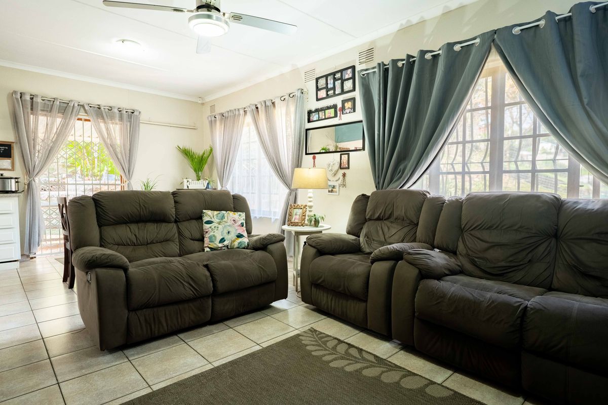 A comfortable living room featuring tiled flooring, a ceiling fan, and large windows with security bars, providing access to the outdoor area.