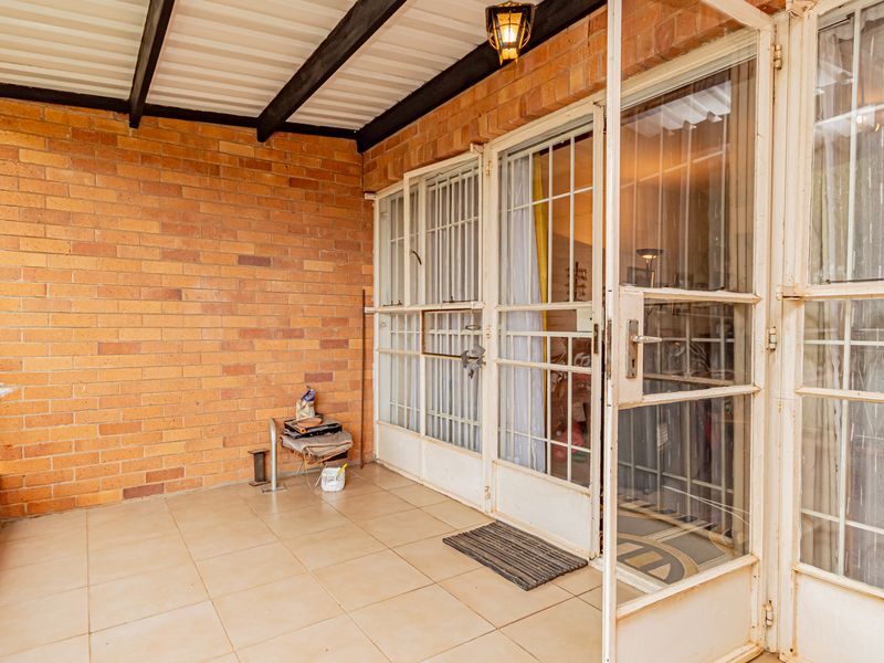 A covered balcony featuring exposed brick walls, tiled flooring, and secure metal gate access to the interior living space.