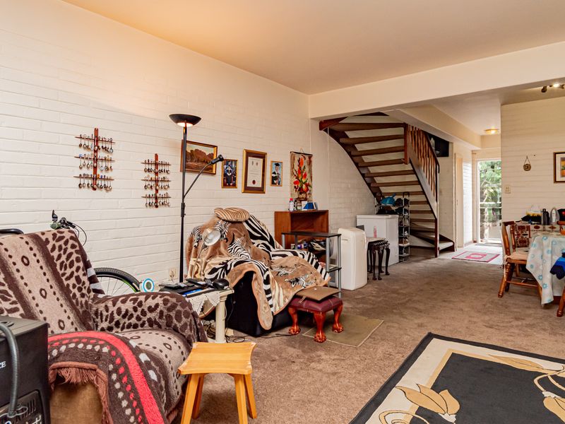 Open plan living and dining area featuring painted brick walls and a timber staircase leading to the upper level.