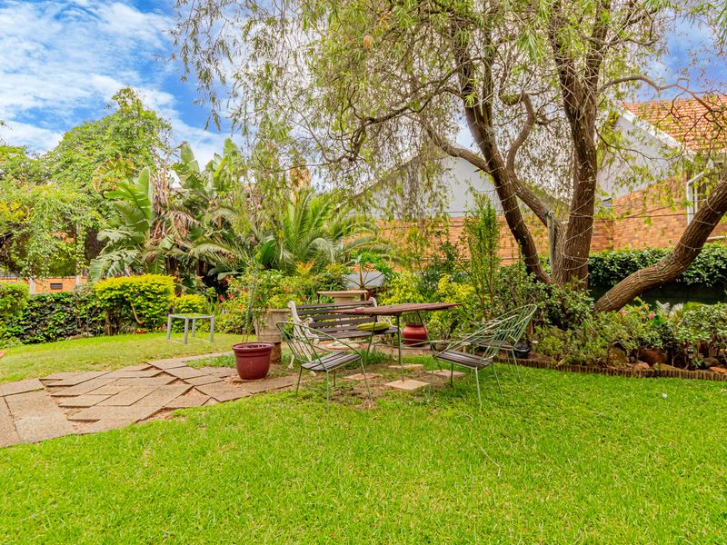 A lush, private garden featuring a paved walkway, mature trees, and established landscaping, providing a tranquil outdoor space for the apartment.