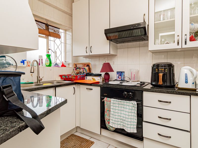 A functional kitchen featuring white cabinetry, granite countertops, a built-in oven with gas hob, and a tiled backsplash with a window for natural light.