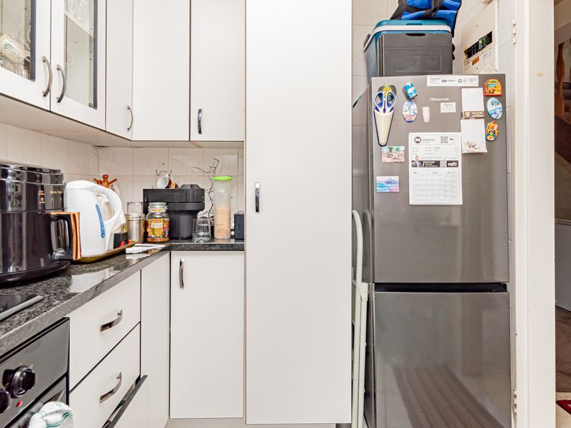 A compact kitchen featuring white cabinetry, dark countertops, and a tiled backsplash, with an adjacent view of the staircase.