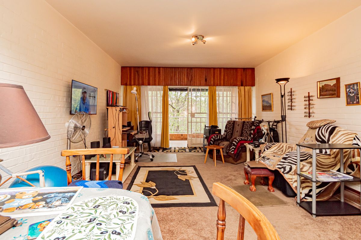 A living room featuring painted brick walls, carpeted flooring, and a sliding glass door leading to an outdoor area.