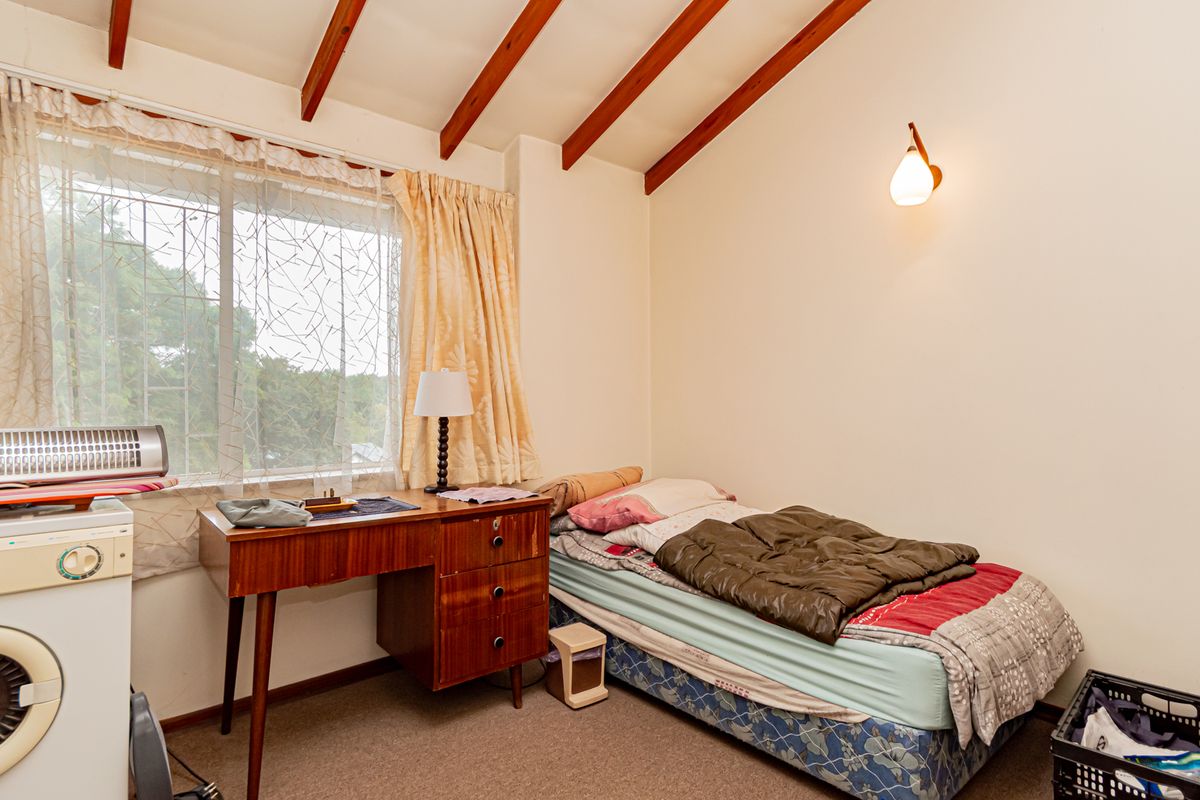 A bedroom featuring exposed timber ceiling beams, a wall-mounted light fixture, and a window with security bars.