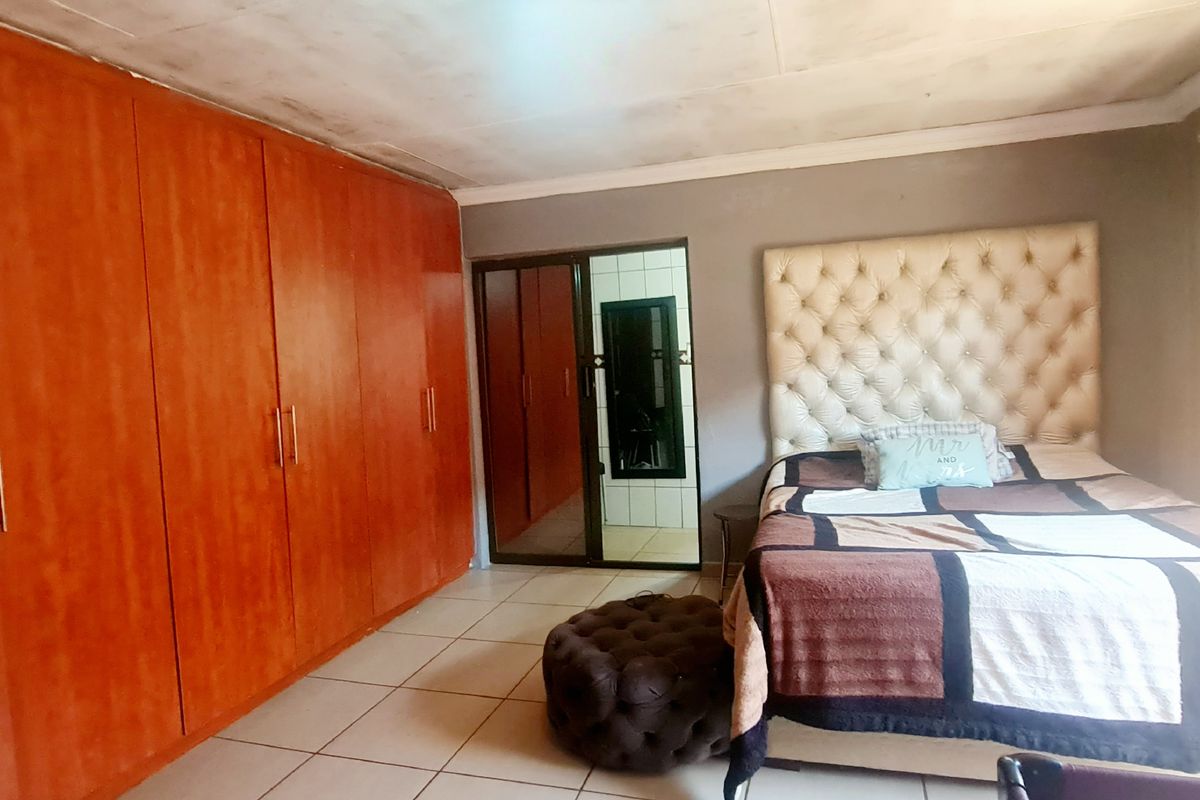 A bedroom featuring built-in wooden cupboards, tiled flooring, and a sliding door, showing signs of ceiling water damage.