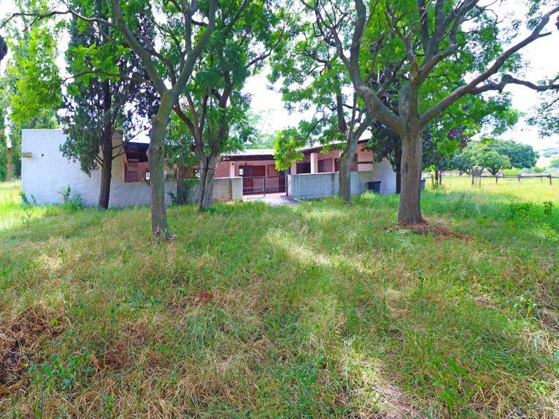 Rear view of the property featuring a masonry boundary wall, metal gate, and covered patio area set within a large, overgrown garden.