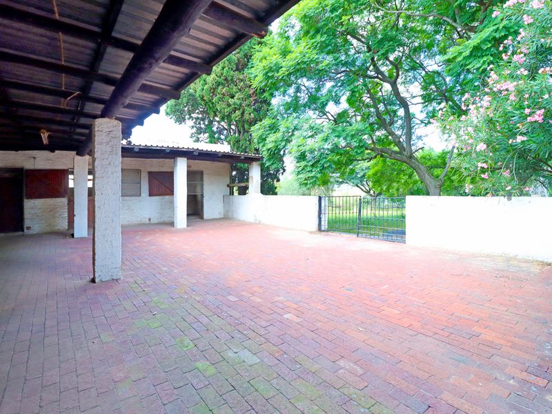 A spacious covered patio area featuring brick paving, masonry support pillars, and direct access to a garden space through a metal gate.