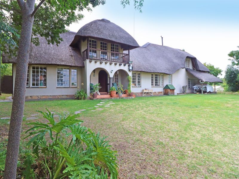 A spacious rear garden view of a traditional thatched-roof house featuring a balcony, arched entrance, and stone base detailing.