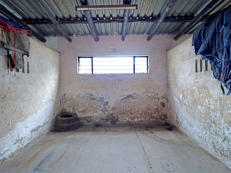 A basic utility space featuring a concrete floor, exposed timber rafters, corrugated metal roofing, and a small window with security bars.