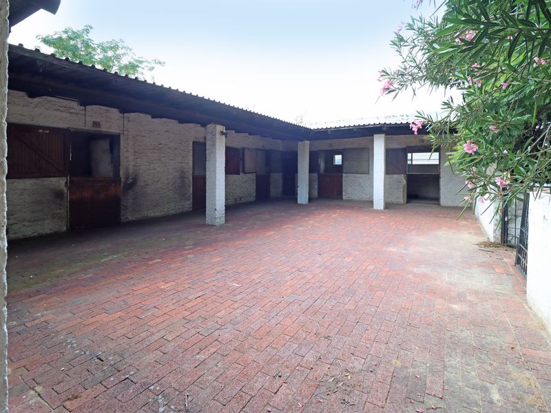 An outdoor utility area featuring brick paving and multiple stable-style stalls with a covered walkway.