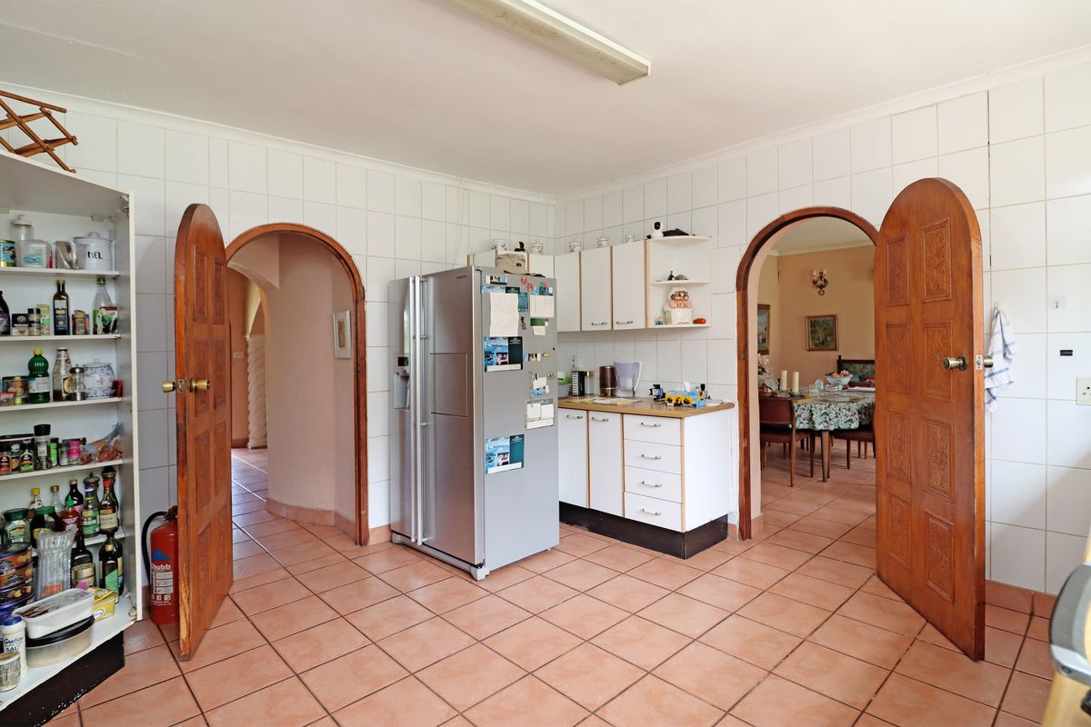 A dated kitchen featuring tiled walls and floors, built-in cabinetry, and distinctive arched doorways leading to adjacent living spaces.