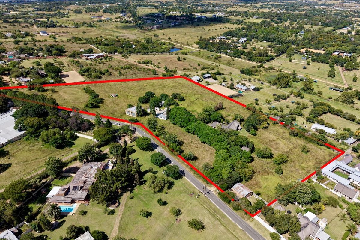 Aerial view of a large, undeveloped plot of land with mature trees and road access, outlined in red for property boundary identification.