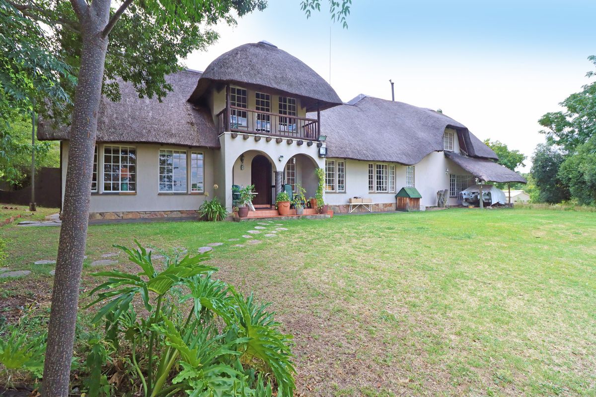 A spacious rear garden view of a traditional thatched-roof house featuring a balcony, arched entrance, and stone base detailing.