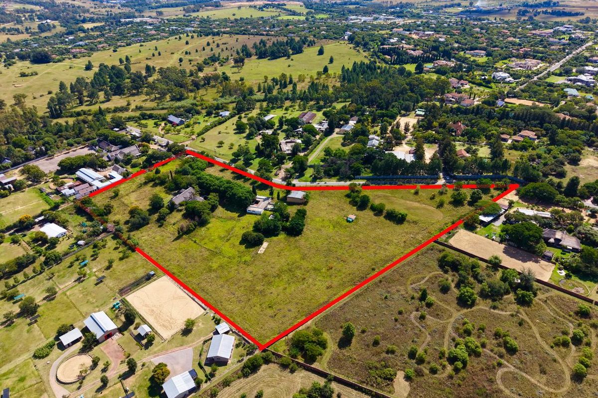 Aerial view of a large residential plot featuring multiple outbuildings, an equestrian arena, and expansive grounds outlined in red.