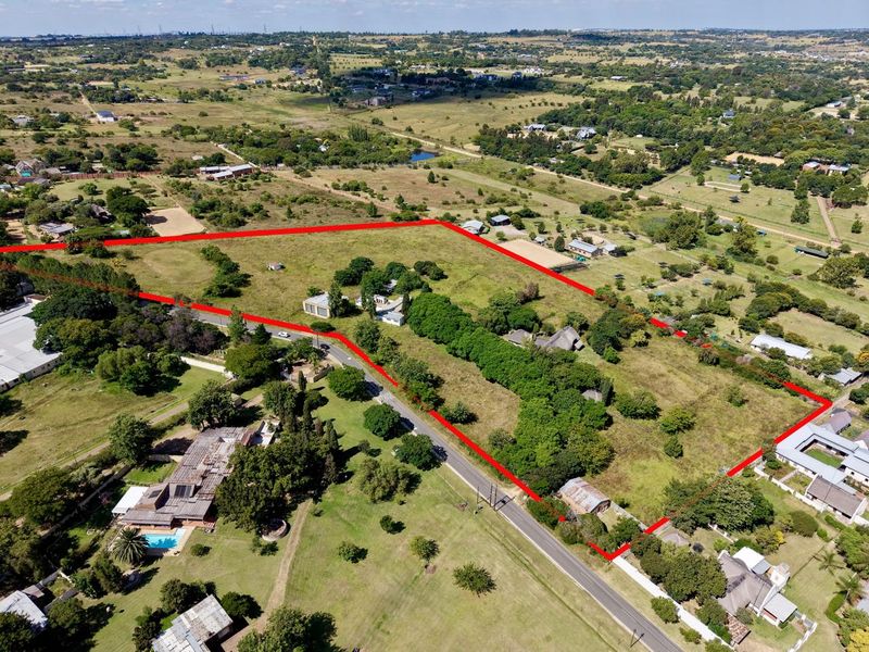Aerial view of a large, undeveloped plot of land with mature trees and road access, outlined in red for property boundary identification.