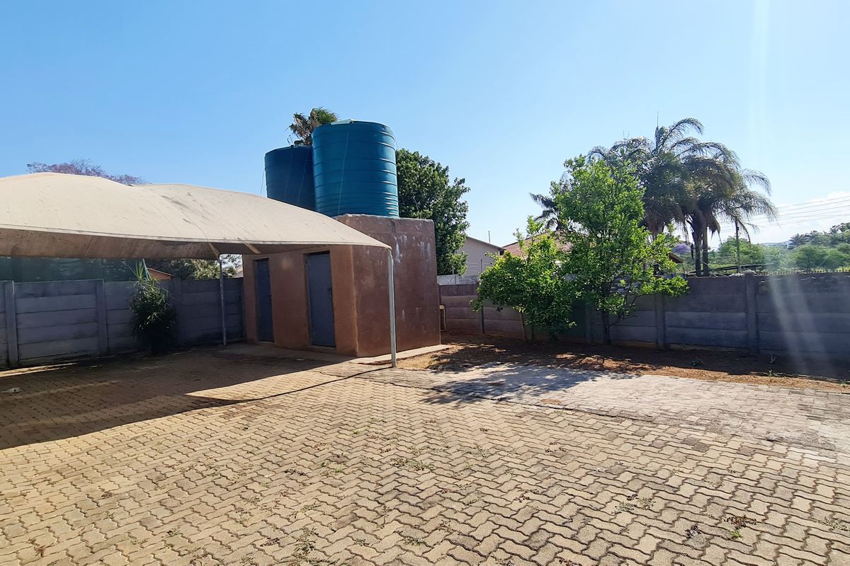 Rear outdoor area featuring a paved driveway, shade sail structure, and elevated water storage tanks enclosed by a precast concrete boundary wall.