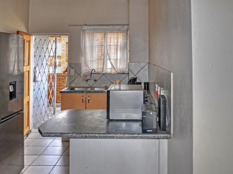 A functional kitchen featuring laminate countertops, built-in cabinetry, a stainless steel sink, and direct access to an outdoor area through a security gate.