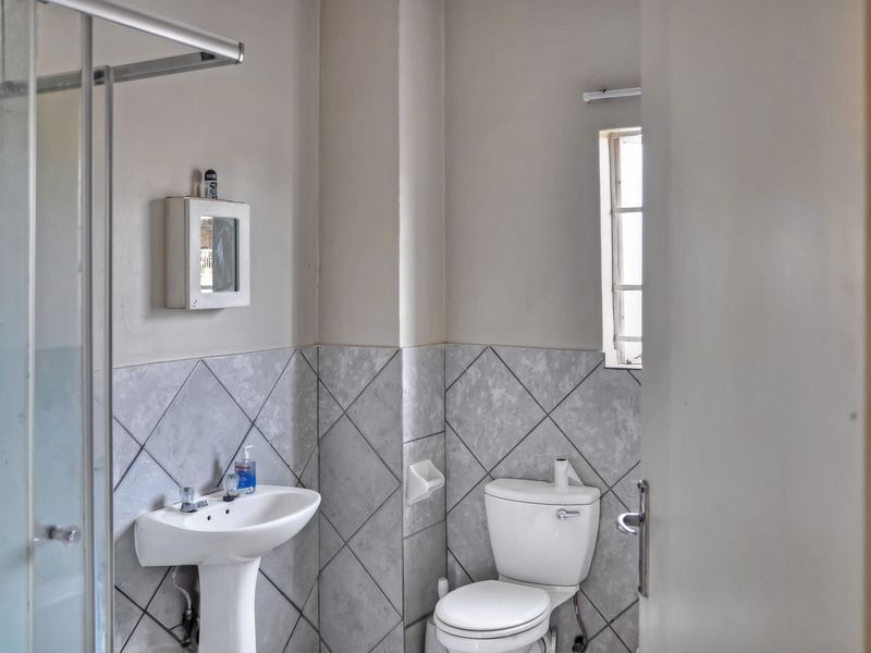 A functional bathroom featuring a pedestal basin, toilet, and shower enclosure with neutral wall tiling.