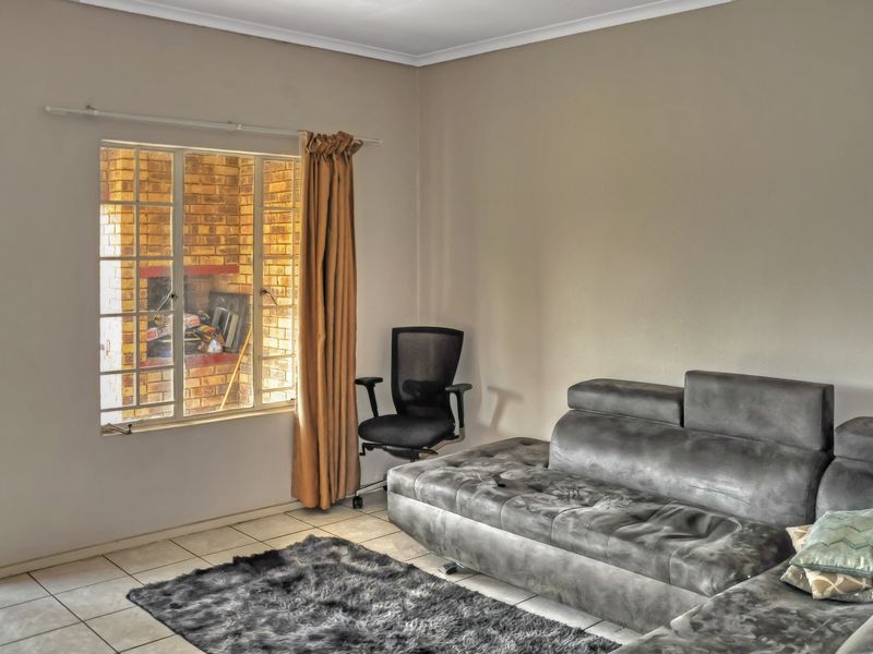 A living room featuring tiled flooring and a window with security bars, offering a functional space with neutral wall finishes.