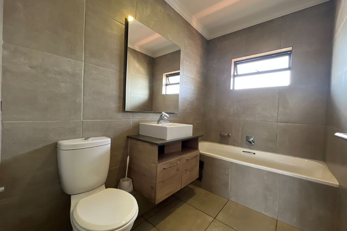 Modern bathroom featuring large format wall tiles, a floating vanity with a vessel sink, a bathtub, and a wall-mounted mirror.