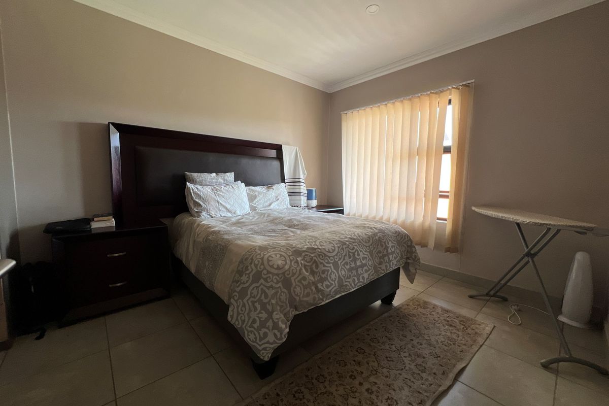 A spacious bedroom featuring neutral wall tones, tiled flooring, and vertical window blinds, providing a comfortable and functional living space.