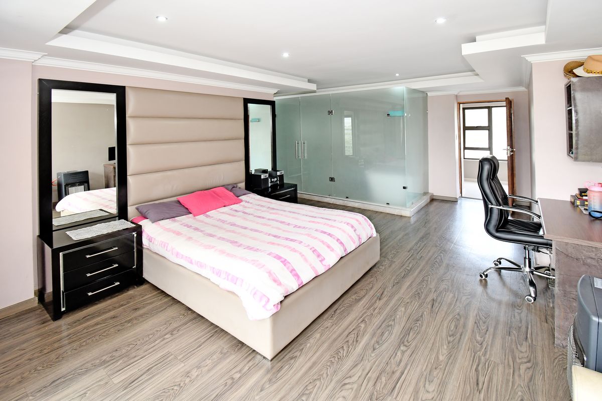 Spacious bedroom featuring modern laminate flooring, recessed ceiling lighting, and a unique glass-enclosed en-suite bathroom.