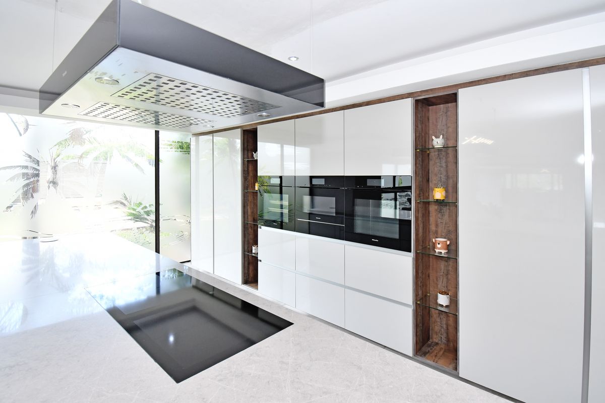 Modern kitchen featuring high-gloss cabinetry, integrated Miele appliances, a large overhead extractor fan, and sleek stone flooring with garden views.