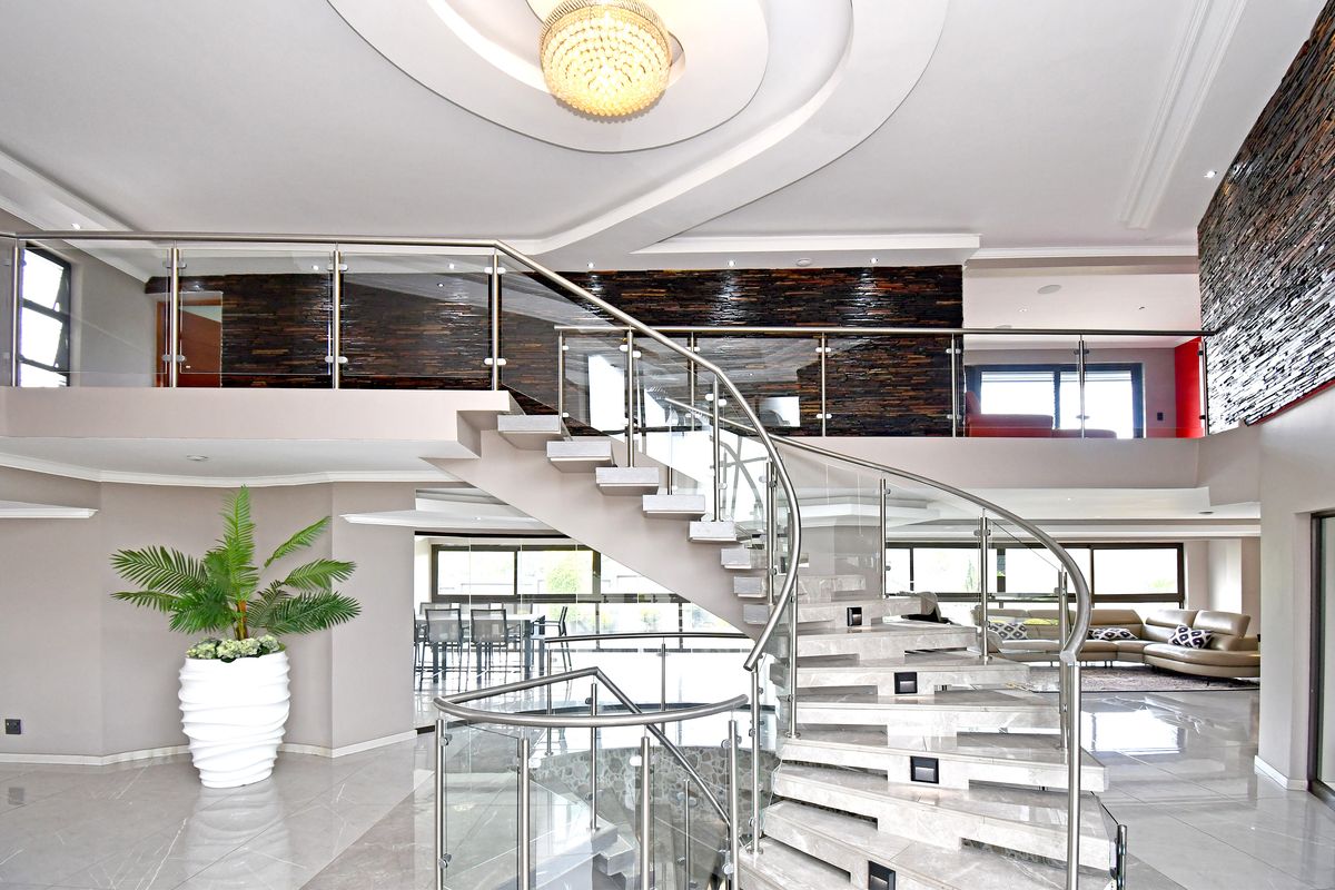 Spacious open-plan living area featuring a grand curved staircase with glass balustrades, stone feature walls, and elegant recessed ceiling lighting.