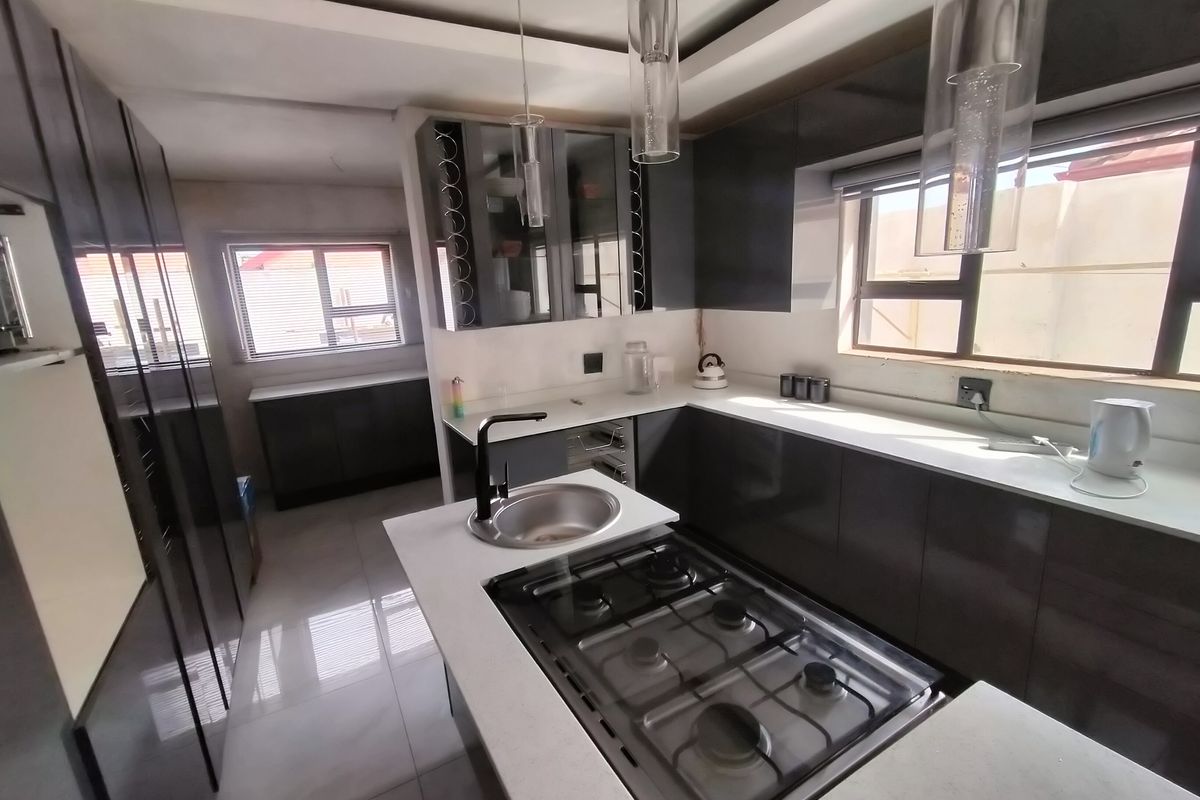Modern kitchen featuring high-gloss cabinetry, stone countertops, a central gas hob, and sleek pendant lighting in a bright, open layout.