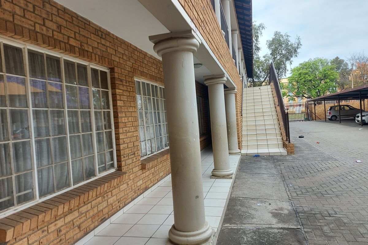 Exterior view of an apartment building featuring a brick facade, covered patio with concrete columns, and an external staircase leading to upper levels.