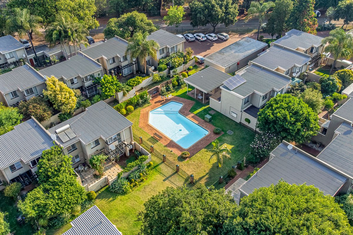 Aerial view of a townhouse complex featuring a communal swimming pool, well-maintained gardens, and residential units with tiled roofs and solar installations.