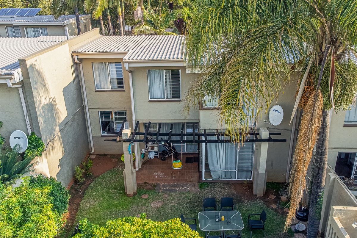 Aerial view of the townhouse rear elevation featuring a covered patio with a pergola, sliding glass doors, and a private garden area.