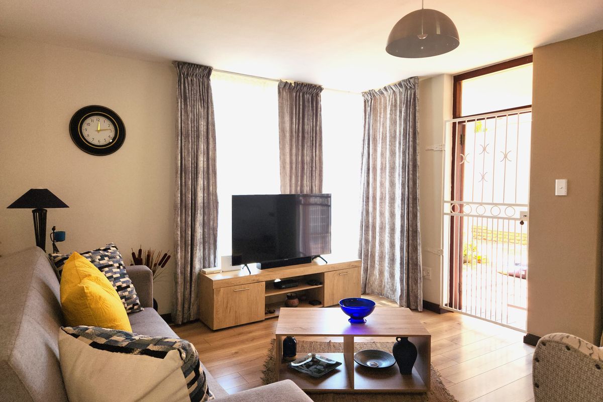 A well-maintained living room featuring laminate flooring, neutral walls, and direct access to an outdoor area through a secure metal gate.