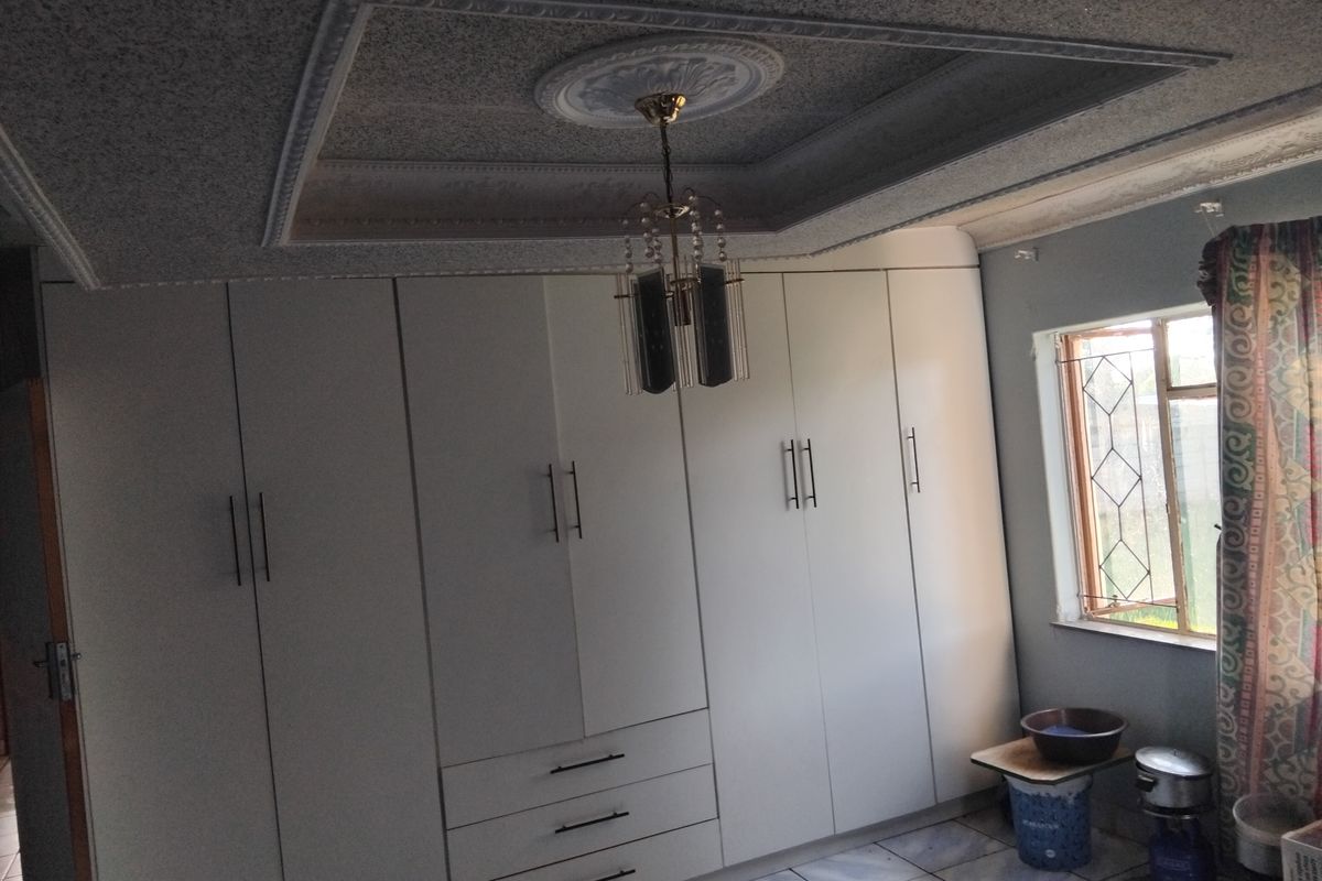 A bedroom featuring extensive built-in cupboards, tiled flooring, and a decorative coffered ceiling with a central light fixture.