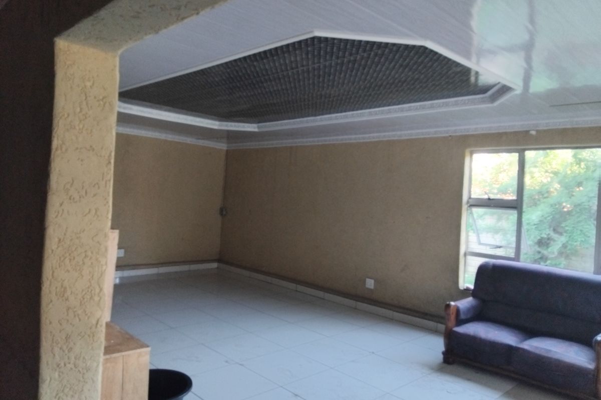 A spacious living area featuring tiled flooring, a unique recessed ceiling design, and textured walls, offering a blank canvas for interior updates.