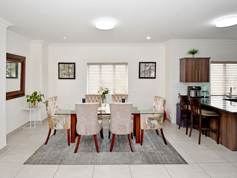 Spacious open-plan dining and kitchen area featuring modern cabinetry, granite countertops, tiled flooring, and ample natural light through venetian blinds.