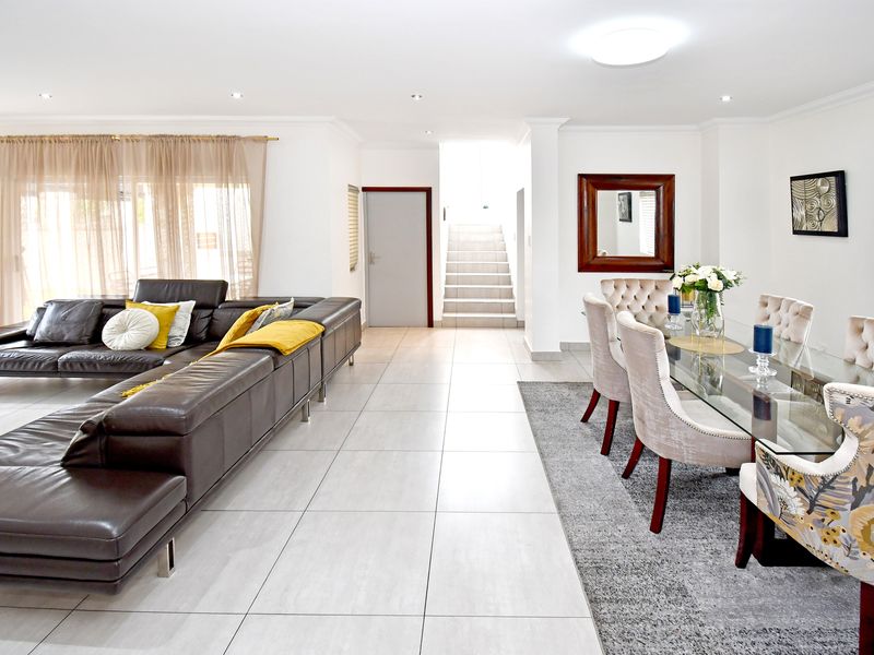 Spacious open-plan living and dining area featuring neutral tiled flooring, recessed lighting, and a central staircase leading to the upper level.